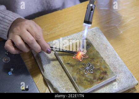 Riscaldamento bruciatore nella produzione e riparazione di gioielli in argento. Torcia di riscaldamento. Un artista femminile realizza gioielli in argento fatti a mano Foto Stock