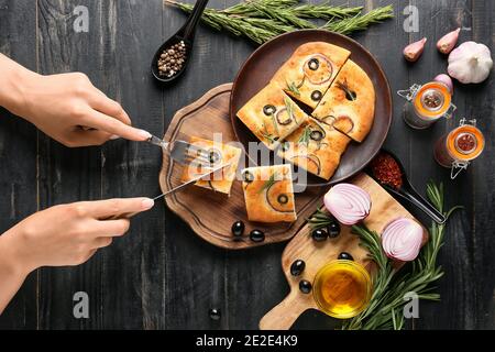 Donna che taglia la tradizionale focaccia italiana su sfondo ligneo Foto Stock