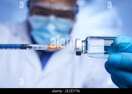 Primo piano di scienziato afro-americano che interagisce con siringa e flaconcino di vetro di vaccino liquido in laboratorio. Foto Stock