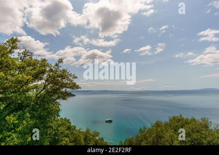 piccolo yacht in acqua cristallina blu con verde alberi in primo piano e cielo blu nuvoloso in croazia Foto Stock