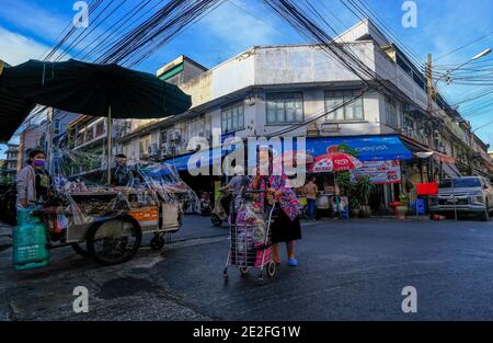 Una donna anziana spinge il suo carrello lungo una strada a Chinatown, Bangkok Foto Stock