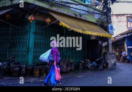 Una donna in colorato abbigliamento viola cammina lungo un vicolo a Talat noi, Bangkok, Thailandia Foto Stock