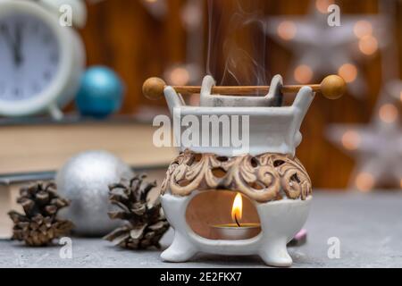 Lampada aromatica in ceramica d'epoca per aromaterapia in composizione invernale. Fiamma della candela e vapore d'olio essenziale. Primo piano, messa a fuoco selettiva, vista nebbia. Foto Stock