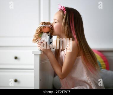 Felice bambina in casa vestiti e fascia gioca con la sua bambola preferita la bacia nel suo letto a casa Foto Stock