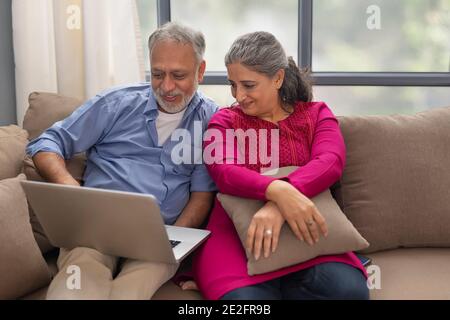 UNA COPPIA SENIOR SEDUTA INSIEME E FELICEMENTE UTILIZZANDO UN COMPUTER PORTATILE Foto Stock