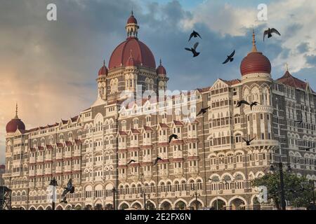 L'iconico Taj Mahal Palace Hotel a Colaba, Mumbai, India, sotto le nuvole drammatiche e con alcuni dei piccioni sempre presenti che volano in primo piano Foto Stock