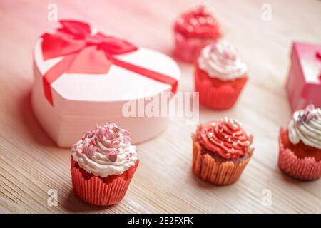 Composizione del giorno di San Valentino. Cupcake con panna montata e spruzzi a forma di cuore, scatola regalo a forma di cuore Foto Stock