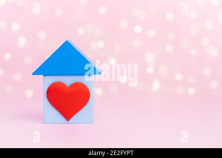 Casa in legno blu con cuore rosso su sfondo bokeh rosa con copy-space. Concetto di casa dolce. Foto Stock