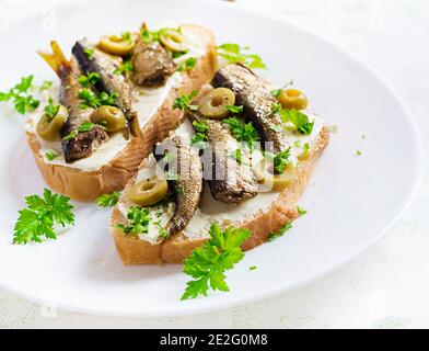 Sandwich - Smorrebrod con spratti, olive verdi e burro su tavola leggera. Cucina danese. Foto Stock