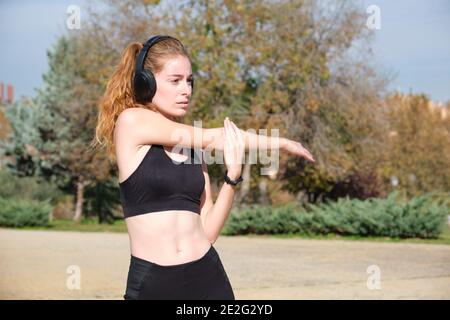 Donna caucasica rossa con cuffie che allungano il braccio. Fitness e sport all'aperto. Foto Stock