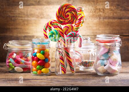 Caramelle colorate, gelatine, lecci, lecci, marshmallows e marmellate in vasi di vetro su tavolo di legno Foto Stock