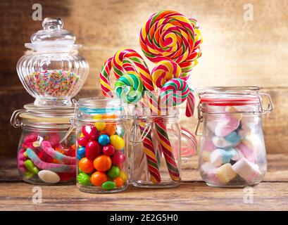 Caramelle colorate, leccarpe e marshmallows in vasi di vetro su tavolo di legno Foto Stock