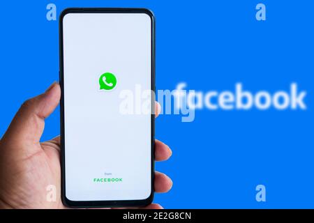 Kathmandu, Nepal - Gennaio 14 2021: L'uomo possiede uno smartphone con il logo WhatApp contro il logo di Facebook sullo sfondo. Foto Stock