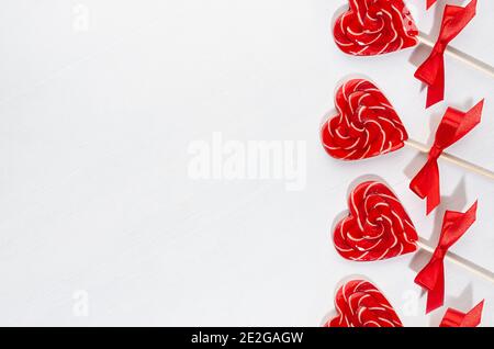 Cuori di lecca rossi con arco di seta su tavola di legno bianco come valentines festivo sfondo giorno, bordo, spazio copia. Foto Stock