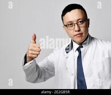 Ritratto di giovane medico urologo o proctologo in bianco abito medico gesturing pollice su segno Foto Stock