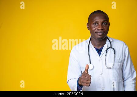 giovane bel medico nero che indossa il suo camice da laboratorio e. appendendo il suo stetoscopio sul collo e dando pollici in su Foto Stock