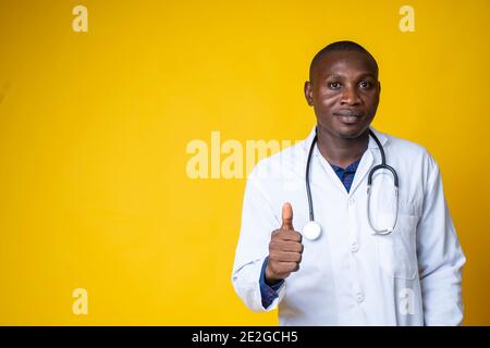 giovane bel medico nero che indossa il suo camice da laboratorio e. appendendo il suo stetoscopio sul collo e dando pollici in su Foto Stock
