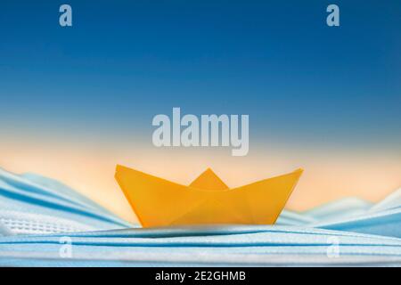 Imbarcazione origami gialla su maschera facciale monouso blu Foto Stock