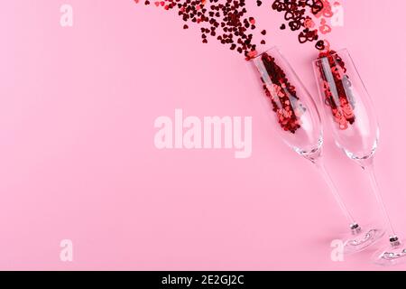 Due bicchieri di champagne pieni di paillettes a forma di cuore su sfondo rosa giorno di San Valentino. Foto Stock