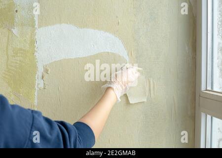 la mano del lavoratore femminile rimuove la vecchia carta da parati dal muro. Il concetto di riparazione, lavori di costruzione Foto Stock