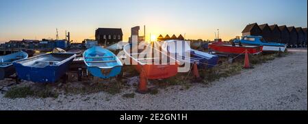 File di barche colorate sulla costa del Nord Kent a Whitstable con le iconiche capanne di pescatori e opere sullo sfondo. Foto Stock