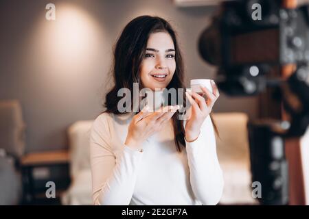 Bella donna di bellezza che promuove crema viso. Famoso blogger. Allegro vlogger femminile sta mostrando prodotti cosmetici, mentre la registrazione video e dando advic Foto Stock