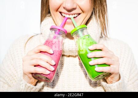 Donna in pullover di lana con 2 bottiglie di frullato o succo di frullato detox rosa e verde fatto in casa. Disintossicazione sana e pulita Foto Stock