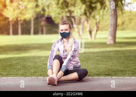 Donna matura con maschera facciale che lega scarpe sportive prima di correre Foto Stock