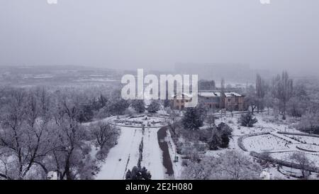 Vista aerea del vecchio parco botanico abbandonato dei tempi dell'Unione Sovietica con alberi e strade tutte coperte di neve verso l'orizzonte nebbia Foto Stock