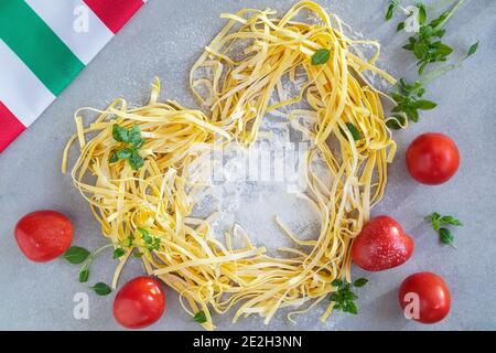 Ingredienti per la cucina italiana, pasta fatta in casa a forma di cuore, farina, pomodori maturi e basilico verde, tovagliolo con tricolore italiano, vista dall'alto. C Foto Stock