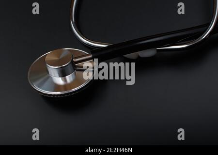 Stetoscopio con tubo in gomma nera su sfondo nero. Strumento medico per terapista e cardiologo. Un dispositivo per l'ascolto di cuore e puls Foto Stock