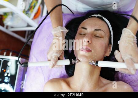 Cosmetologia. Bella donna presso la clinica termale ricevere stimolante trattamento facciale elettrico da terapeuta. Primo piano di Young Female Face durante Microcu Foto Stock