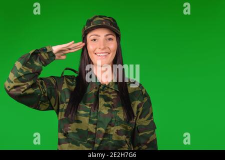 Ritratto di una donna militare caucasica sorridente. Soldato che saluta contro uno sfondo verde con spazio vuoto per la vostra pubblicità Foto Stock
