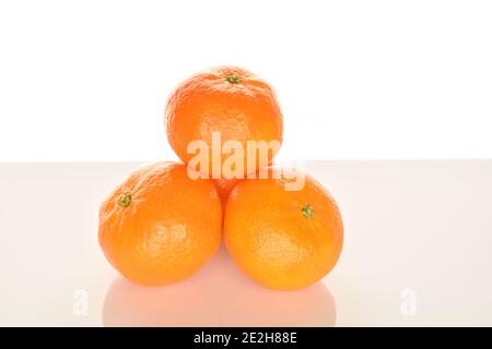 Alcuni tangerini interi di colore arancio brillante e succosi, su sfondo bianco. Il mandarino più vicino, in primo piano in primo piano. Foto Stock