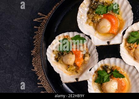 Capesante, limone, aglio, prezzemolo, burro e sale su fondo nero. Chiudete le capesante cotte con caviale e salsa cremosa all'aglio. Ricetta per cucinare Foto Stock