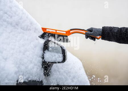 donna con un cigolio pulisce la neve da un'auto parcheggiata nel cortile Foto Stock