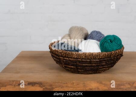 Palle di filato colorate in cesto su tavola di legno su bianco sfondo Foto Stock