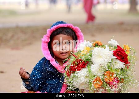 Dhaka, Bangladesh - 14 gennaio 2021: La madre del bambino è un venditore di fiori. Lasciò il bambino con i fiori nel parco e ne andò a fare alcuni Foto Stock