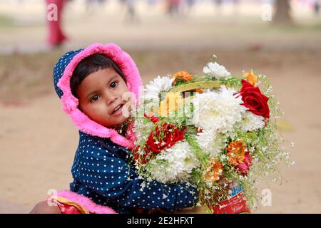 Dhaka, Bangladesh - 14 gennaio 2021: La madre del bambino è un venditore di fiori. Lasciò il bambino con i fiori nel parco e ne andò a fare alcuni Foto Stock