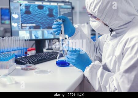 Uomo nel laboratorio di microbiologia contenente la capsula di Petri che lavora con la micropipetta che indossa la tuta. Chimico in laboratorio moderno che fa la ricerca usando il dispenser durante l'epidemia globale con covid-19. Foto Stock