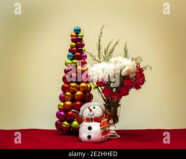 Scena di Natale con fiori pupazzo di neve e albero di natale fatto di decorazioni a sfere decorative lucide Foto Stock