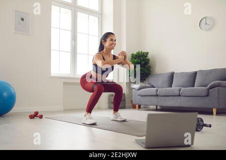 Donna che si allenava con una fascia in gomma davanti a un computer portatile durante una trasmissione di un allenamento fitness. Foto Stock