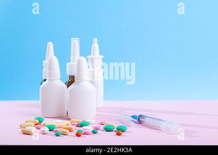 Molti farmaci medici, siringa, spray, flaconi di gocce nasali, sparsi da pillole flacone colorato compresse, capsule su sfondo blu e rosa, hori Foto Stock