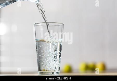 Un bicchiere d'acqua viene versato dalla caraffa in un vetro singolo in un tavolo da cucina Foto Stock