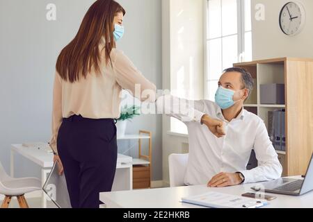 I colleghi in faccia ricoprono le maschere urtare i gomiti come alternativa alla normale stretta di mano Foto Stock