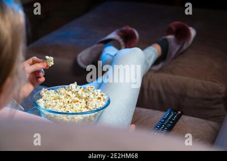 Primo piano di un popcorn che si sveglia a mano da una ciotola mentre si guarda la TV. La persona si siede in un comodo divano e guarda l'Home Cinema al buio. Foto Stock