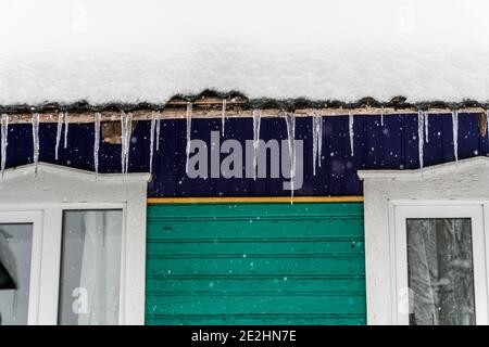 Caduta di ghiaccio icicles appendere sulla casa in inverno, il tetto è coperto di neve, inverno nel villaggio Foto Stock