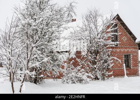 Casa di mattoni dietro gli alberi con neve, un sacco di neve, villaggio in inverno Foto Stock