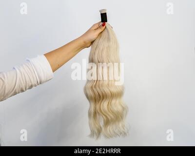 Mano di Famale che tiene un fascio di remy umano naturale biondo estensioni dei capelli su sfondo bianco Foto Stock