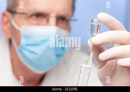 Primo piano del medico che prepara una siringa per la vaccinazione contro covid-19 - mettere a fuoco la siringa Foto Stock